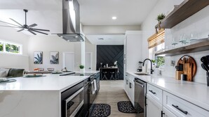Une cuisine moderne avec des meubles blancs, un îlot central et un plan de travail noir. On y trouve également un ventilateur de plafond, une cuisinière et un évier.