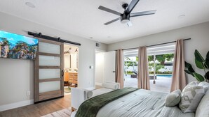 Une chambre moderne dotée d’un grand lit, d’un ventilateur de plafond et d’une porte-fenêtre coulissante donnant sur un balcon avec vue sur la piscine.