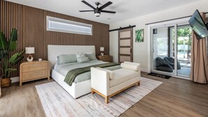 Une chambre à coucher comprenant un lit, des tables de chevet, un ventilateur de plafond, une porte-fenêtre coulissante et une vue sur l’extérieur.