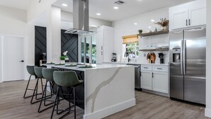 Une cuisine moderne dotée d’un îlot central, de tabourets de bar, d’appareils électroménagers en acier inoxydable et d’une palette de couleurs en noir et blanc.