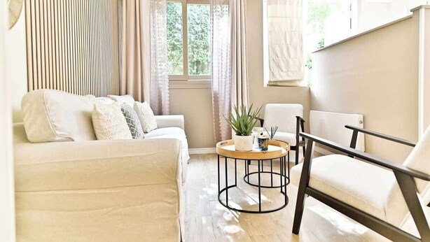 A living room with a sofa, armchair, round coffee table, and curtains. - Charmant appartement Paris 12e (Paris)