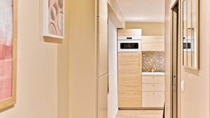 A narrow hallway leading to a kitchen with wooden cabinets, a tiled backsplash, and a stainless steel oven. - Charmant appartement Paris 12e (Paris)