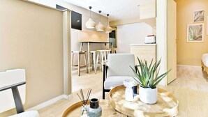A modern living room with a dining area, a kitchen in the background, and a plant on a side table. - Charmant appartement Paris 12e (Paris)