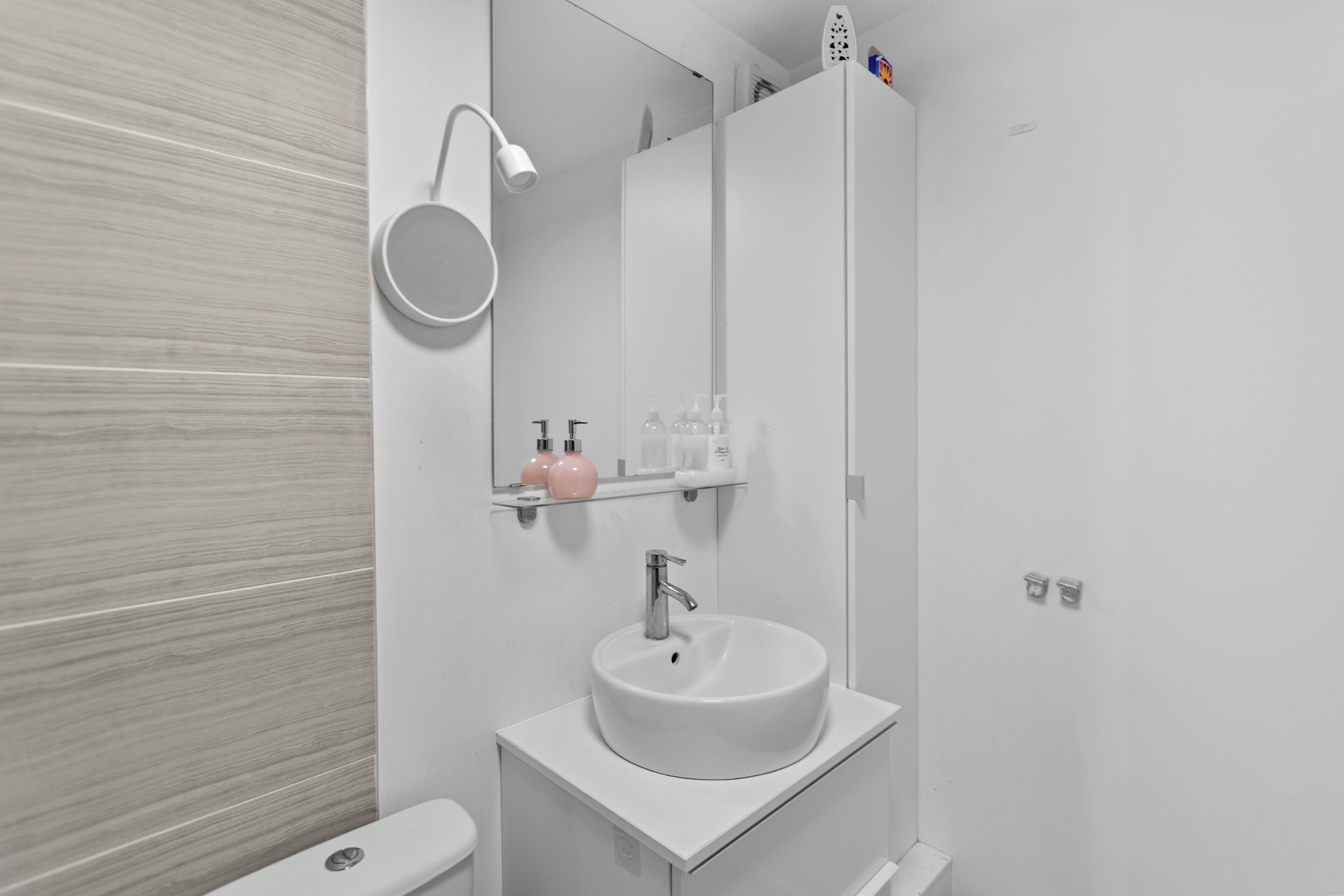 Un baño moderno con un lavamanos blanco, un espejo redondo y una zona de ducha.