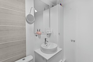 A modern bathroom with a white sink, a round mirror, and a shower area. - Cozy 2 Bed Apartment Close to Lcy & Excel (London)