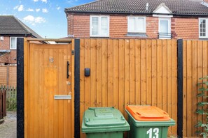 A wooden gate with a number 13 sign, two green bins with number 13, and a brick house in the background. - Cozy 2 Bed Apartment Close to Lcy & Excel (London)