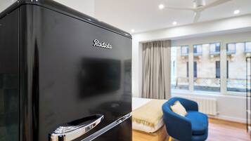 A black refrigerator with the brand name "Radiola" in a modern room with a blue chair, a bed, and a window with curtains.