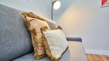 Un sofá gris con tres almohadones, uno beige y dos marrones, con detalles de flecos.