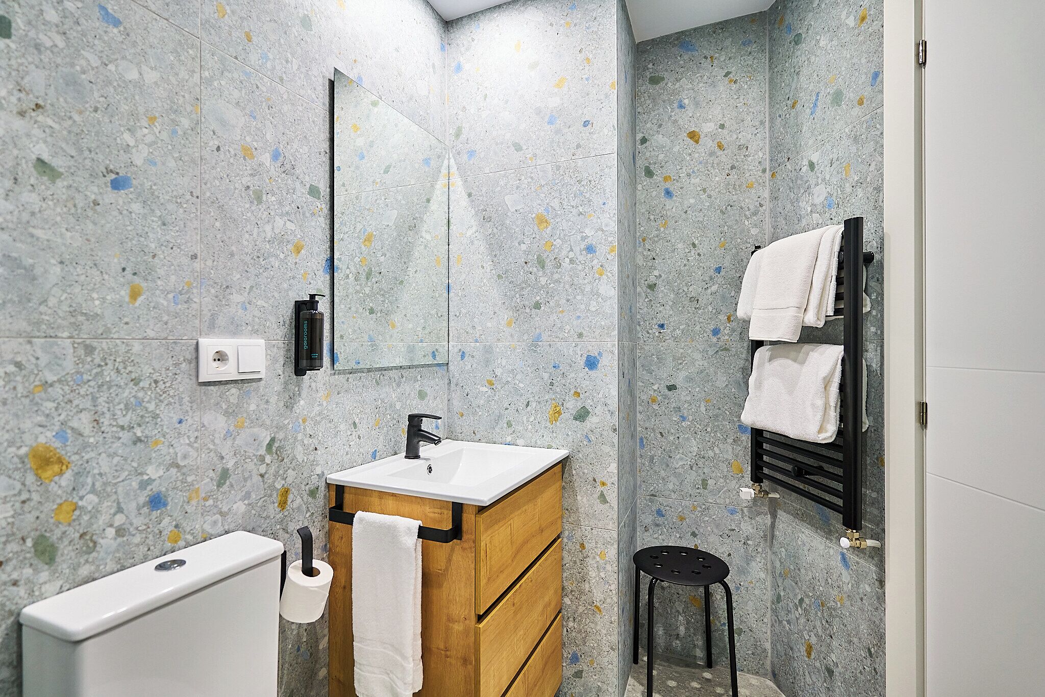 Un baño con lavamanos de mármol, tocador de madera, inodoro y barra para toallas.
