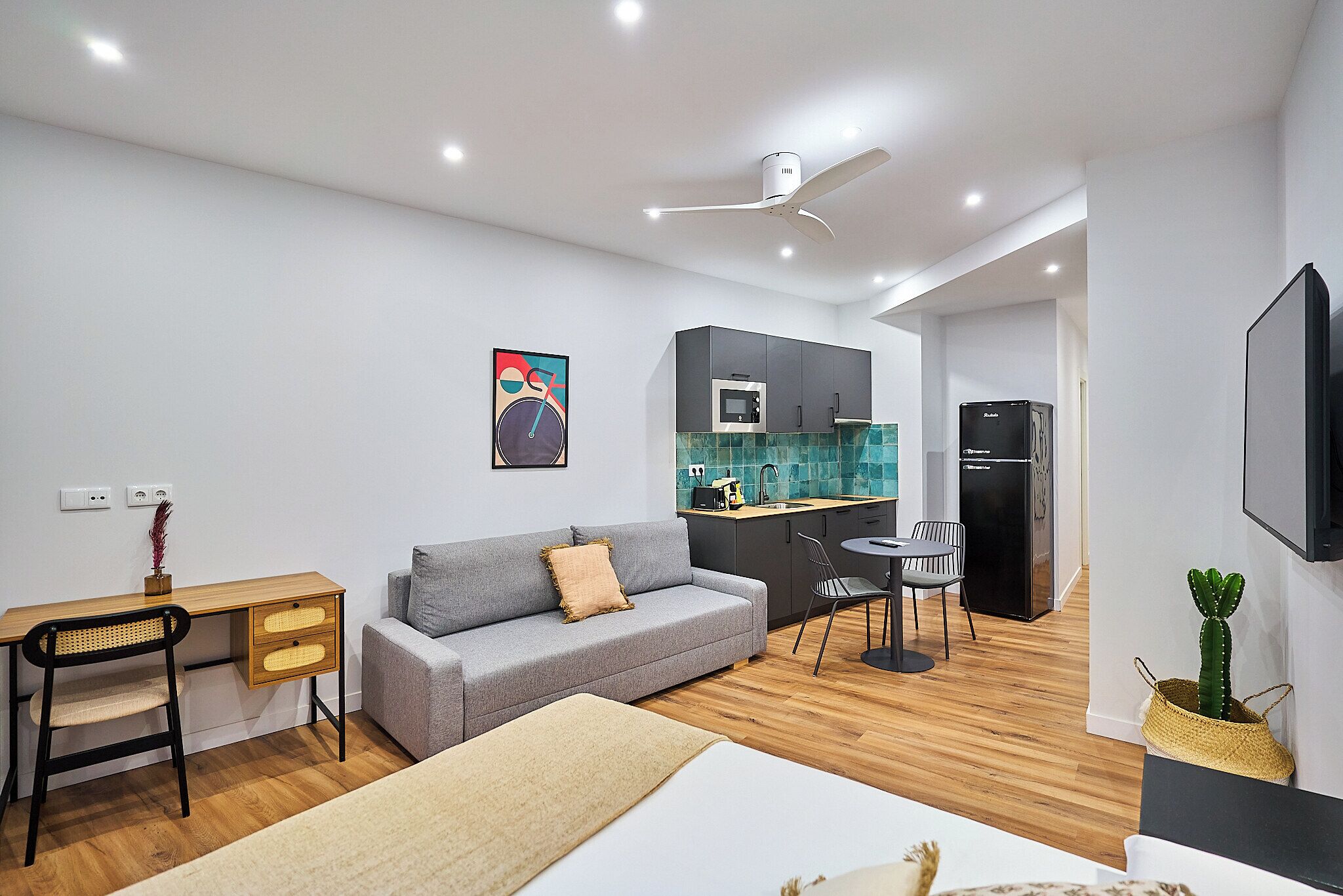 A modern, compact living space with a kitchenette, a sofa, a desk, and a dining area.