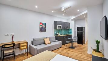 A modern, compact living space with a kitchenette, a sofa, a desk, and a dining area.