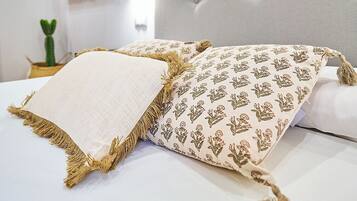 A neatly made bed with patterned pillows and a decorative throw, a flat-screen TV mounted on the wall, and a small potted plant on the nightstand.