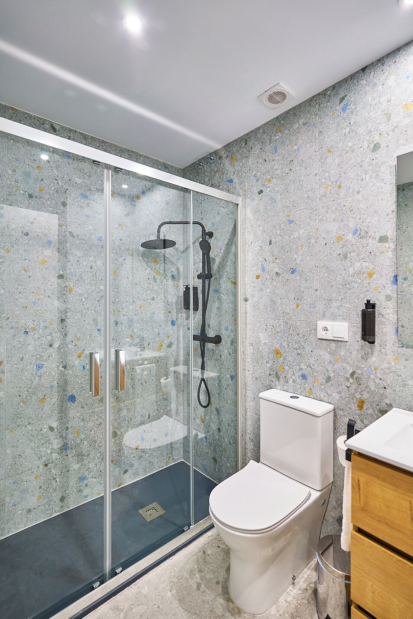 A modern bathroom with a glass-enclosed shower, a toilet, and a wooden cabinet.