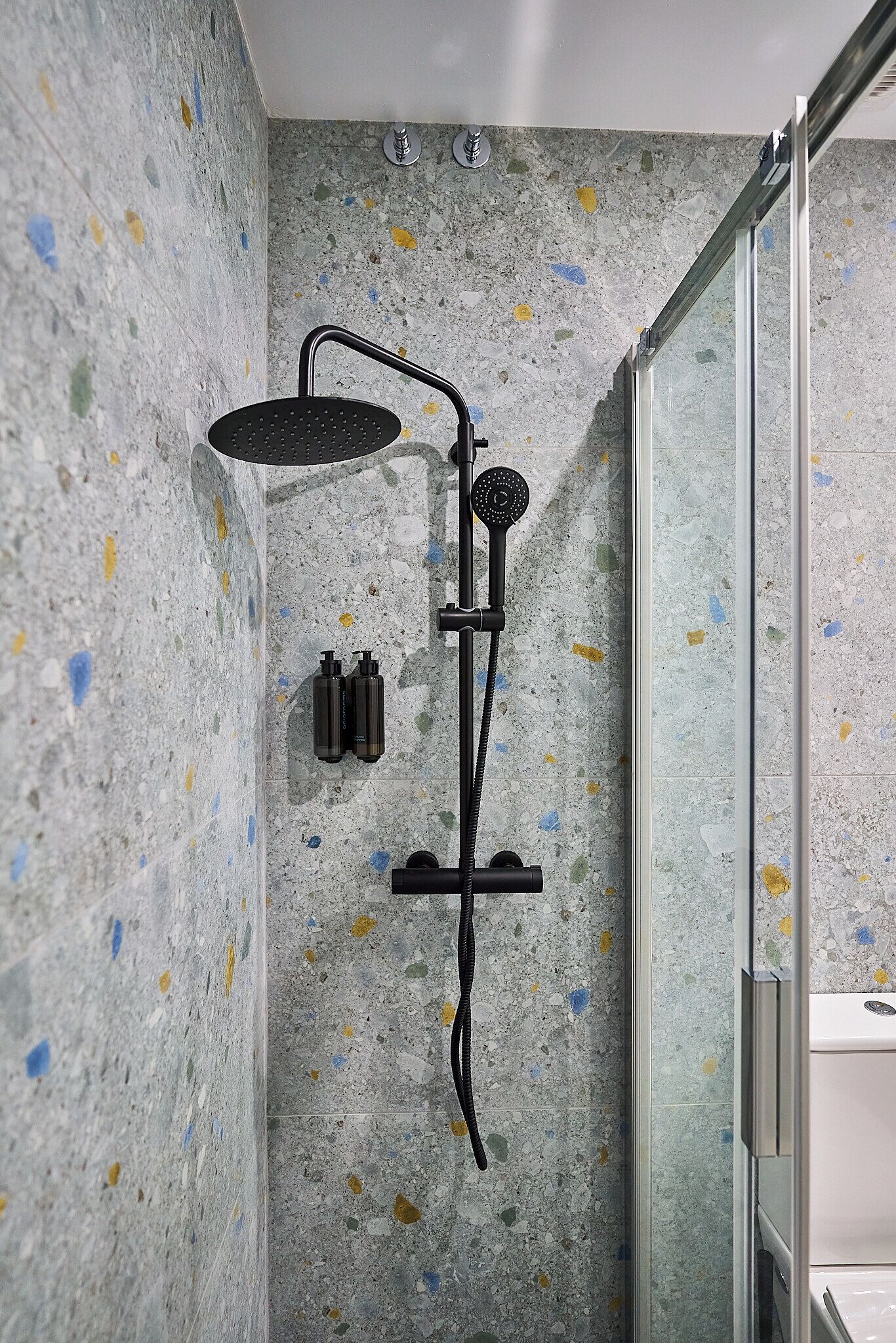 A shower with a rain showerhead, a handheld showerhead, and two bottles of shampoo.