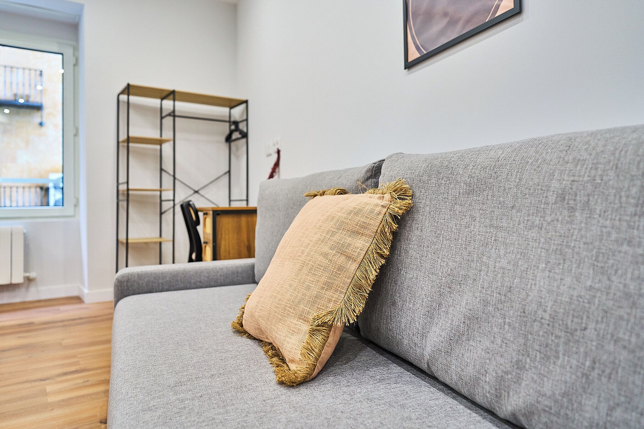 A grey sofa with a beige cushion and a wooden shelf unit against a white wall.