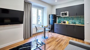 Een compacte keuken met moderne apparatuur, een zithoek met tafel en stoelen, en een groot raam met gordijnen.