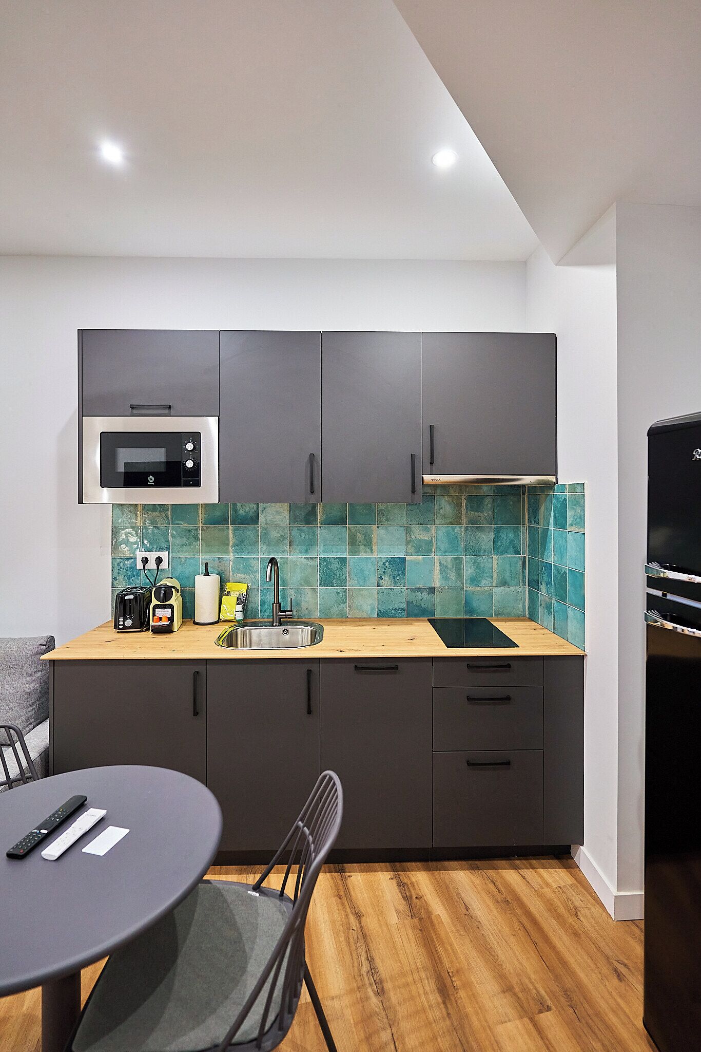 A modern kitchen with grey cabinets, a microwave, a sink, and a wooden countertop.