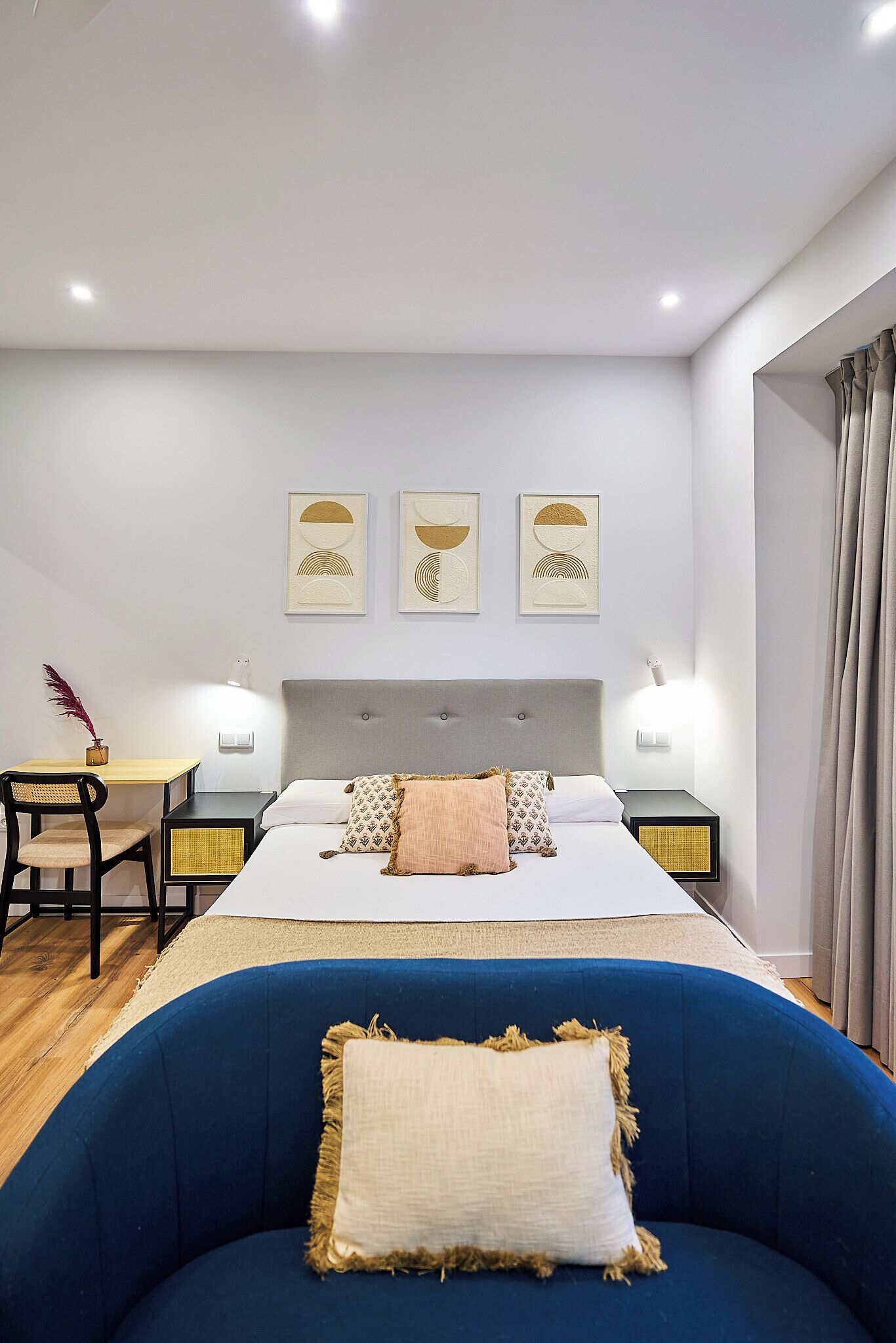 Una habitación de hotel moderna con una cama grande, un escritorio con una silla y un sillón azul.