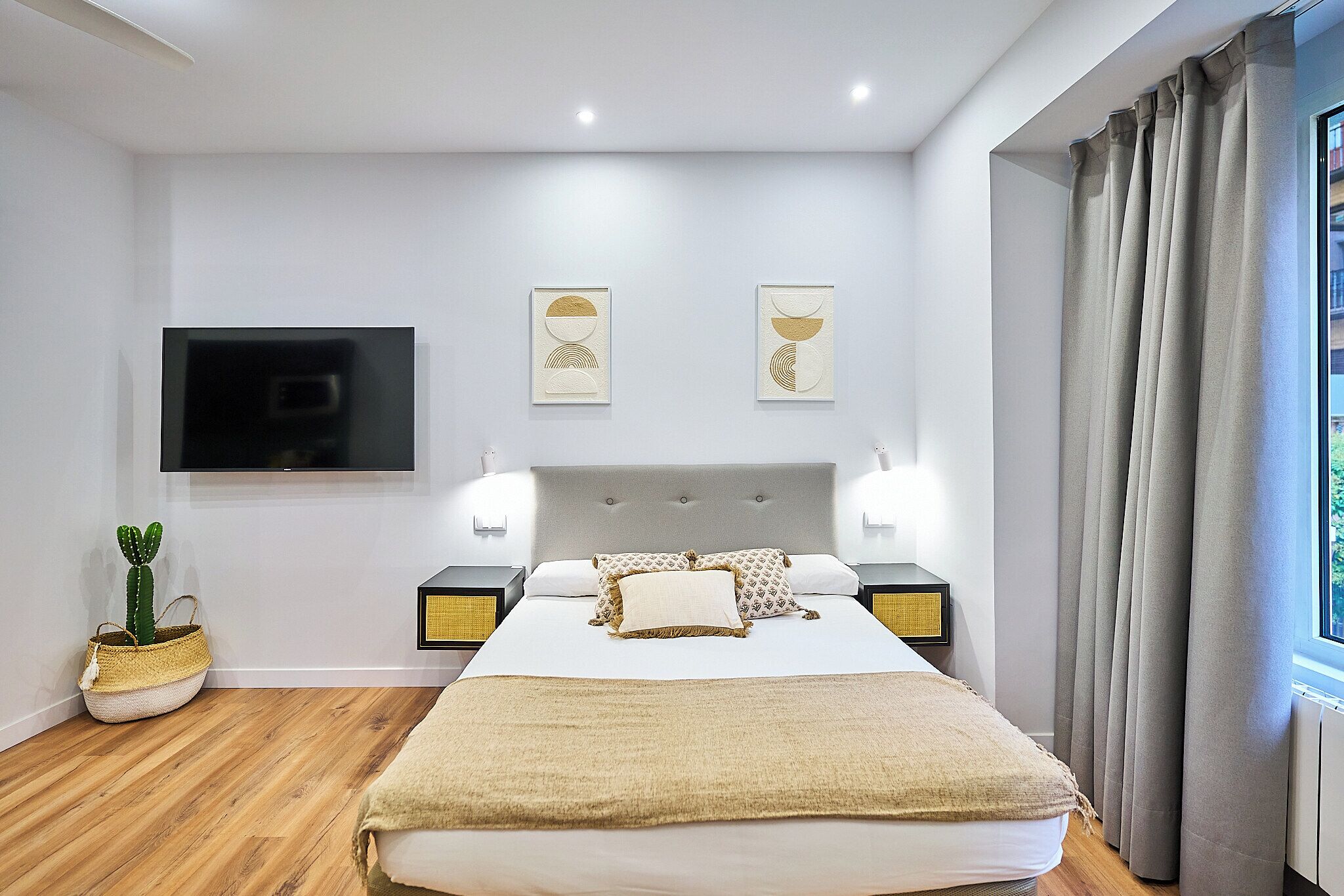A modern bedroom with a large bed, bedside tables, a flat-screen TV, and artwork on the wall.