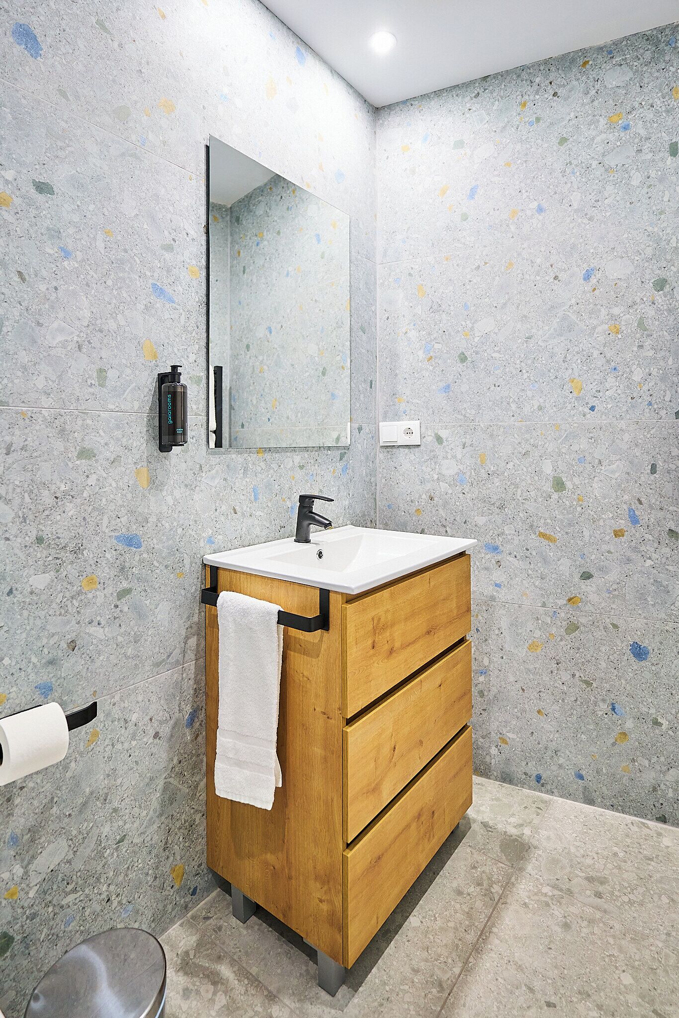 A bathroom with a wooden vanity, a white sink, a mirror, and a towel hanging on the vanity.