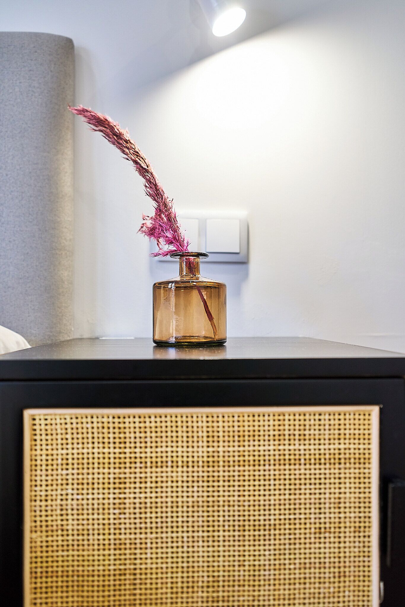 Een nachtkastje met een vaas met gedroogde bloemen en een lamp.