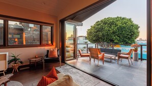 A modern living room with a large window, a sofa, a coffee table, and a view of a balcony with outdoor furniture. - Ocean View Craftsman Home - Great Location + Walk to Beach (Encinitas)