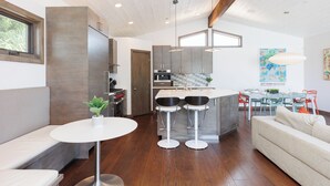 A modern kitchen with a central island, bar stools, and a dining area with a table and chairs. - Ocean View Craftsman Home - Great Location + Walk to Beach (Encinitas)