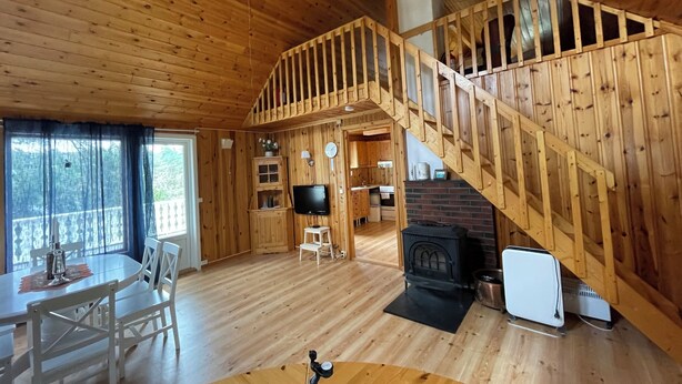 A wooden cabin interior with a dining area, a living room, a kitchen, and a staircase.