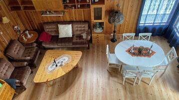 A cozy room with a wooden floor, a brown sofa, a round coffee table, and a white dining table with chairs.