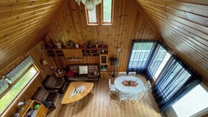 A wooden cabin interior with a dining table, chairs, a sofa, and a coffee table.