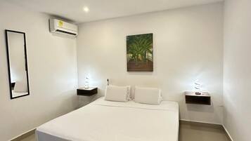 Una habitació d'hotel moderna amb un llit gran, parets blanques, un aparell d'aire condicionat, un quadre i taules de nit amb làmpades.