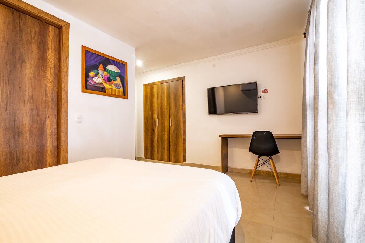 A bedroom with a bed, a desk, a chair, a television, and a wardrobe.