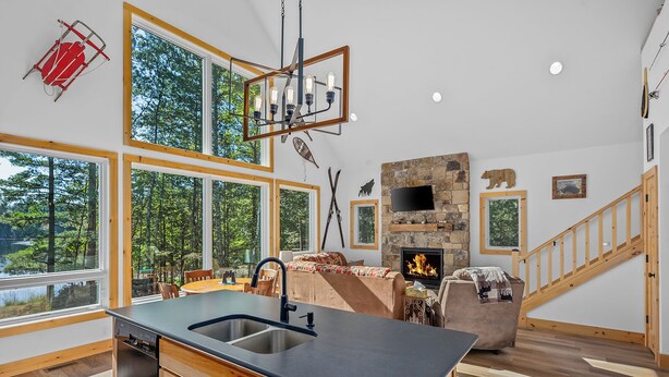 Una cocina moderna con una isla grande, una chimenea y un comedor con vistas al bosque.