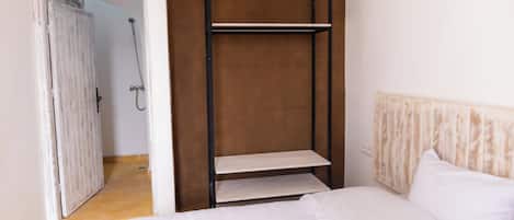 Un dormitorio con cama, cabecera de madera, armario con estantes y baño visible a través de una puerta abierta.