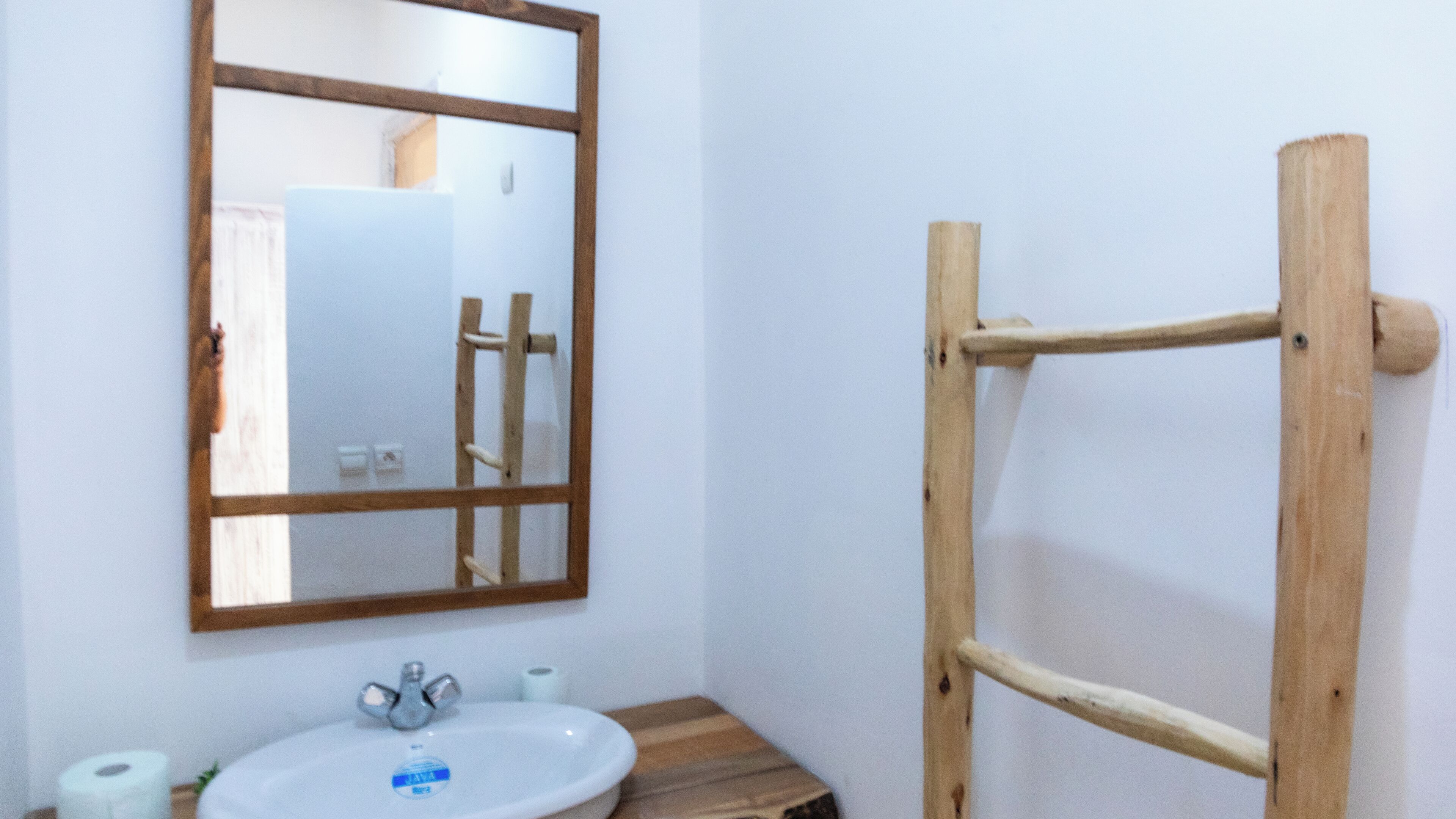 Une salle de bain avec une échelle en bois, un lavabo avec un miroir et deux rouleaux de papier toilette.
