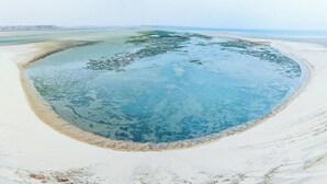 Una extensa masa de agua ovalada rodeada de arena blanca, con un centro azul cristalino y un borde arenoso.