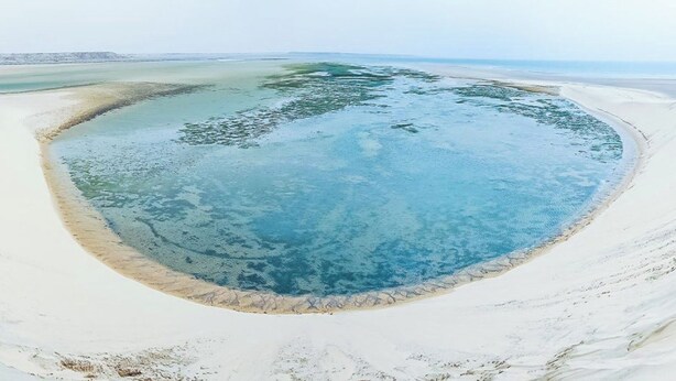 A large, oval-shaped body of water surrounded by white sand, with a clear blue center and a sandy perimeter. - Dakhla Roof Top (Dakhla)