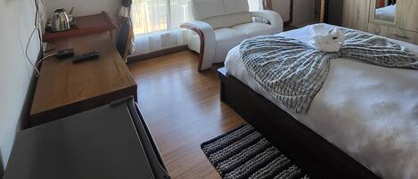 A hotel room with a bed, a desk with a TV, a ceiling fan, and a wardrobe.