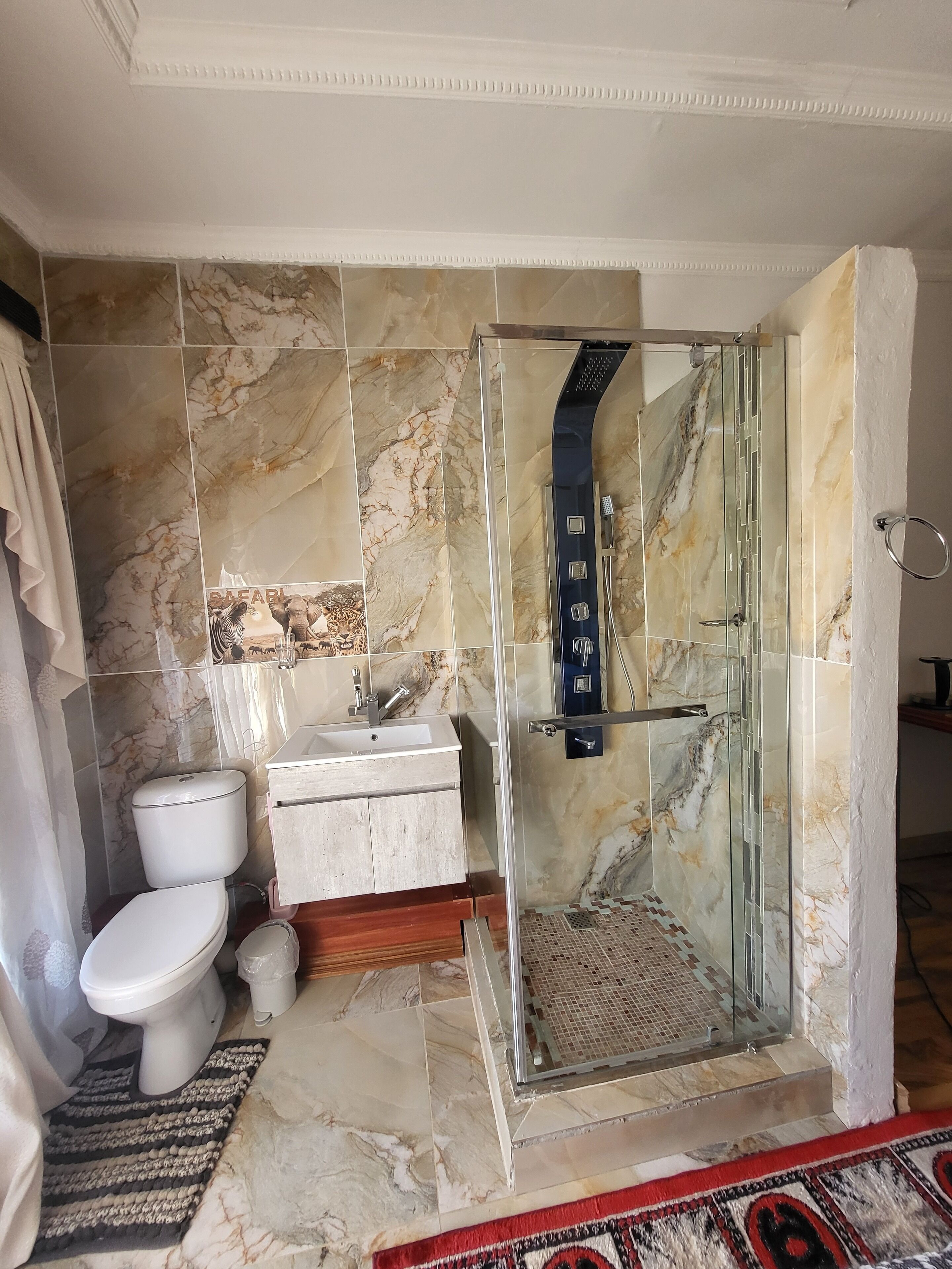 Ein Badezimmer mit einer Glaskabine zur Dusche, Toilette, Waschbecken und einer Wand mit Marmorfliesen.