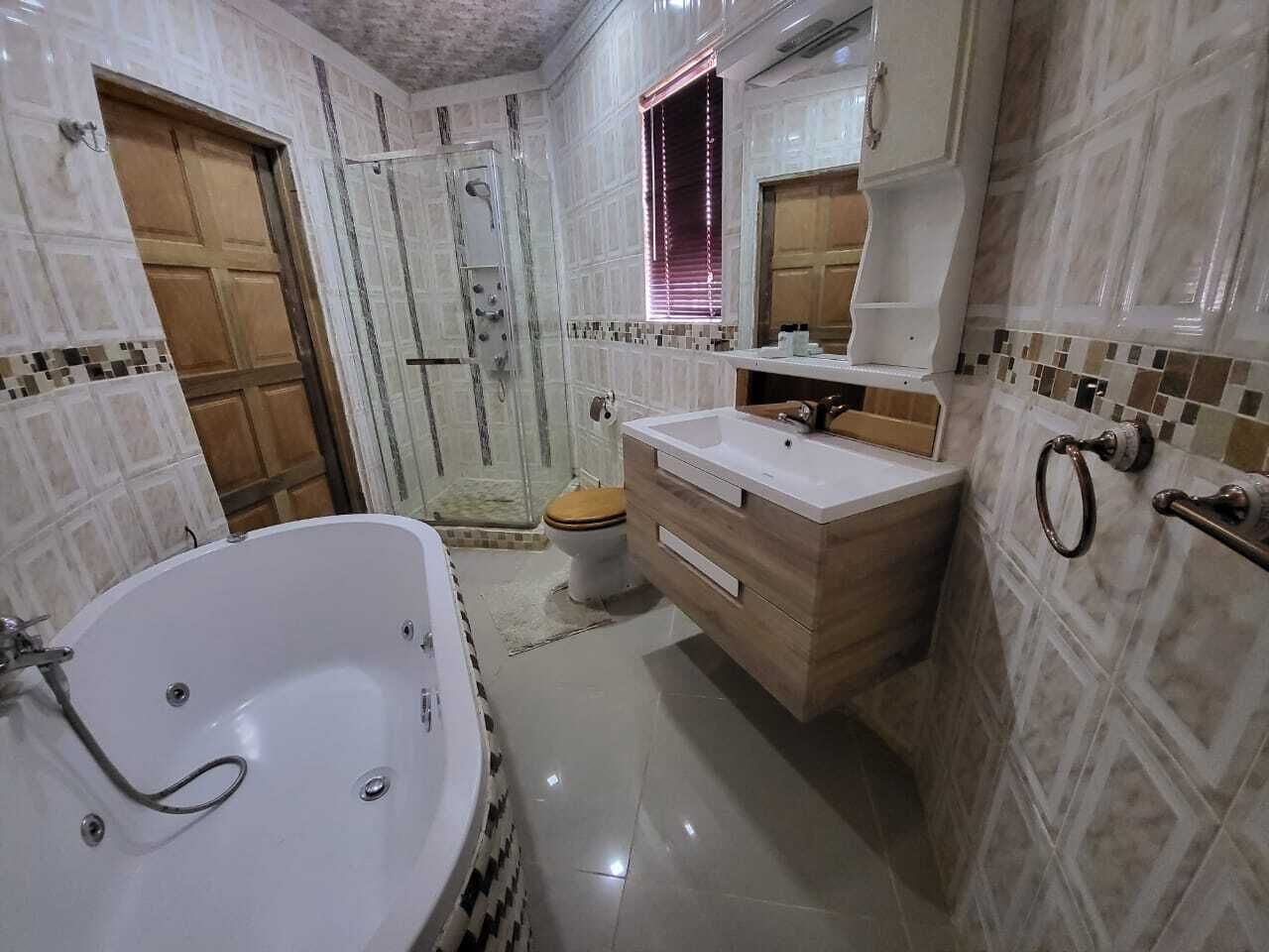 A bathroom with a large bathtub, a wooden vanity, a toilet, and a shower area.