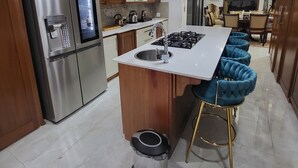 Una cucina moderna con elettrodomestici in acciaio inossidabile, mobili in legno, un piano di lavoro in marmo e un angolo bar con sgabelli imbottiti blu.
