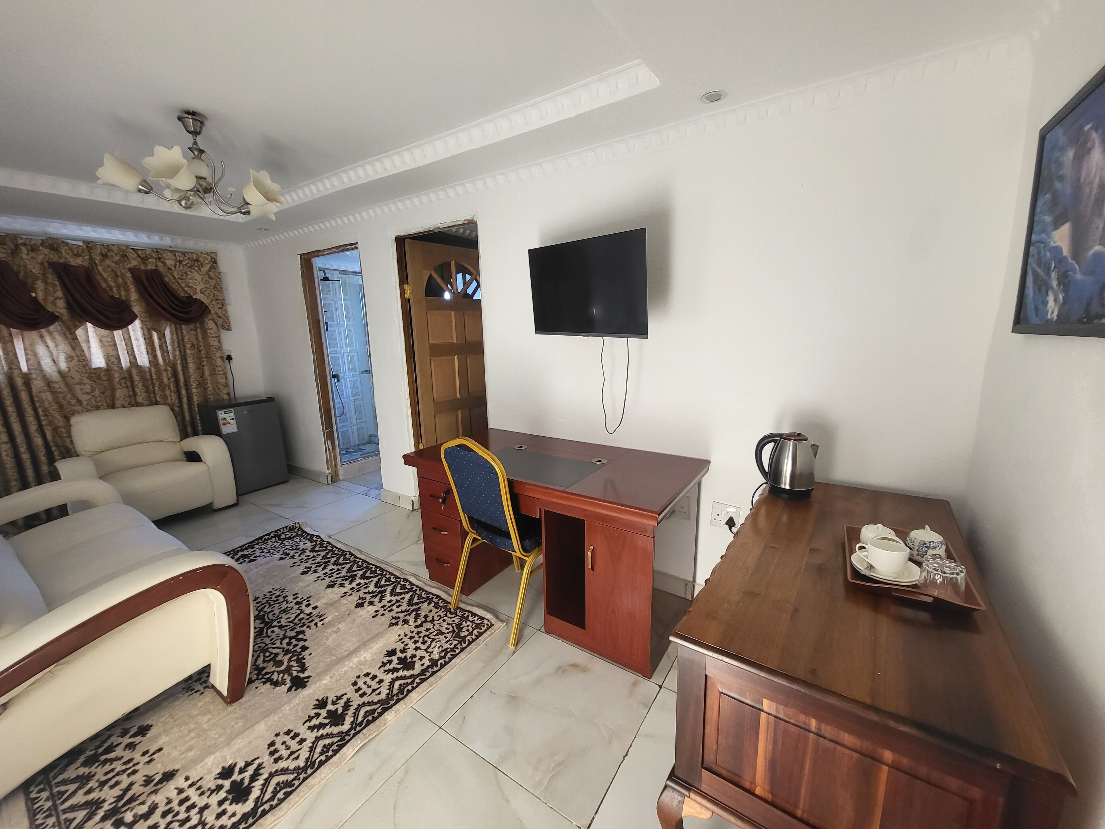 A living room with a sofa, a wooden desk, a television, and a coffee table with a kettle and cups.