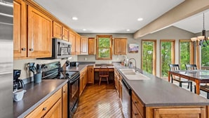 A kitchen with wooden cabinets, a stainless steel refrigerator, a microwave, a stove, and a dining area with a table and chairs. - Wanderlust •HotTub •Spa Room w/Sauna •2 King Suites (Gatlinburg)