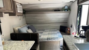 Un intérieur de camping-car compact comprenant un lit, un coin cuisine et un espace salon.