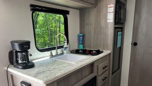 A compact kitchenette with a coffee maker, sink, and stove. - Cozy Camper in Charming Whittier with Heat & AC (Whittier)