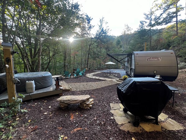 A camping site with a Coleman RV, outdoor seating, and a grill.