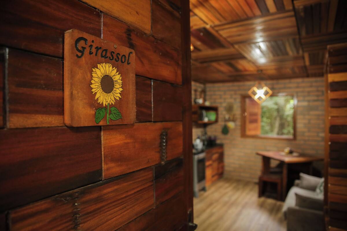A wooden interior with a sign reading "Girassol," a wooden wall, a wooden ceiling, a television, a window, and a sofa.