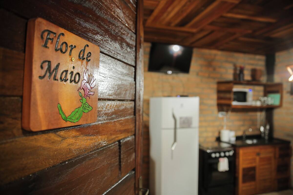A wooden wall with a sign reading "Flor de Maio" and a kitchen area with a refrigerator, microwave, and wooden cabinets.
