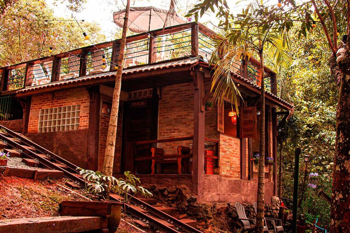 A rustic wooden building with a balcony, surrounded by lush greenery and a staircase leading up to it.