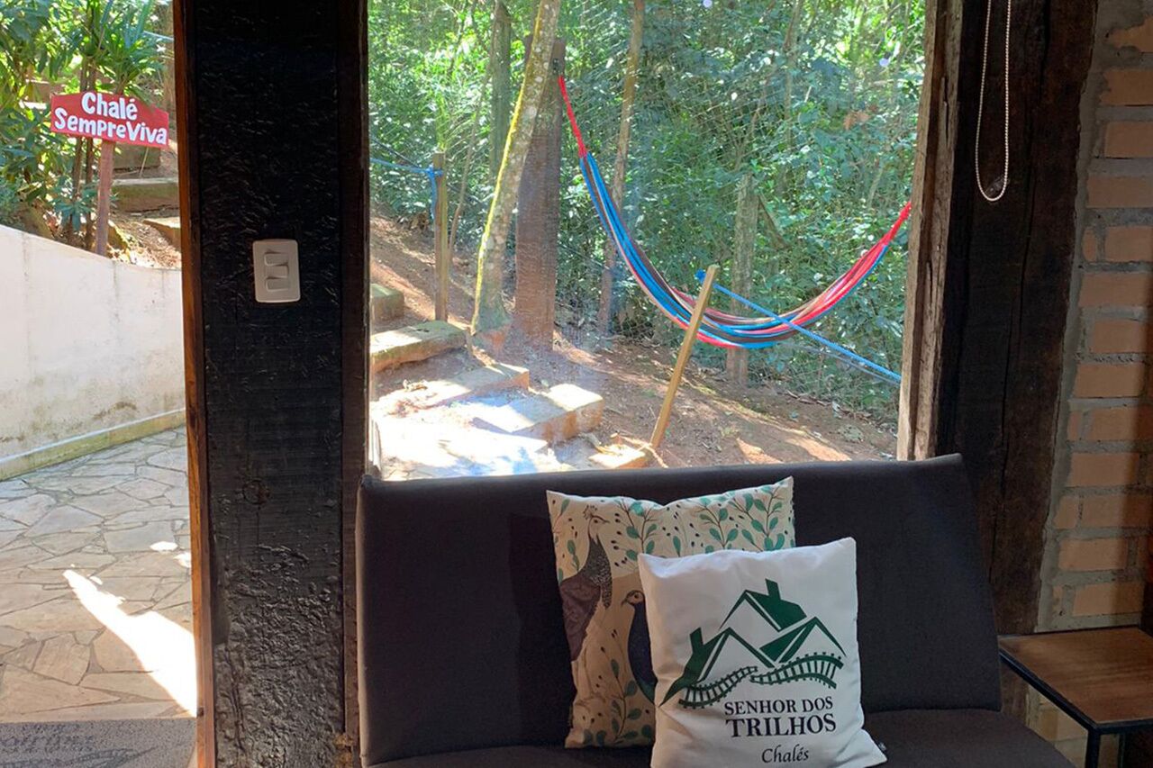 A window seat with a hammock, a pillow with a logo, and a neon sign outside.